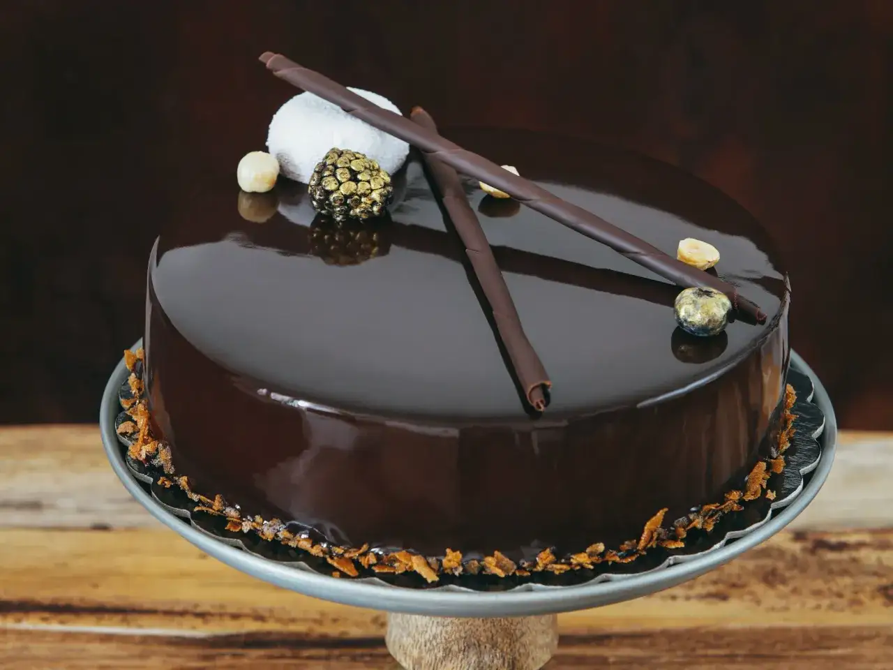 Torta con glassa al cioccolato lucida, decorata con riccioli di cioccolato, nocciole e una sfera dorata.