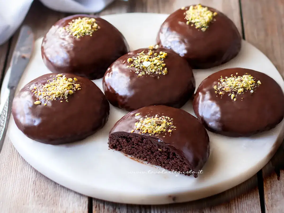 Dolci rotondi glassati al cioccolato, guarniti con granella di pistacchi. Sembrano deliziosi, quasi un salame al cioccolato in versione tortino.