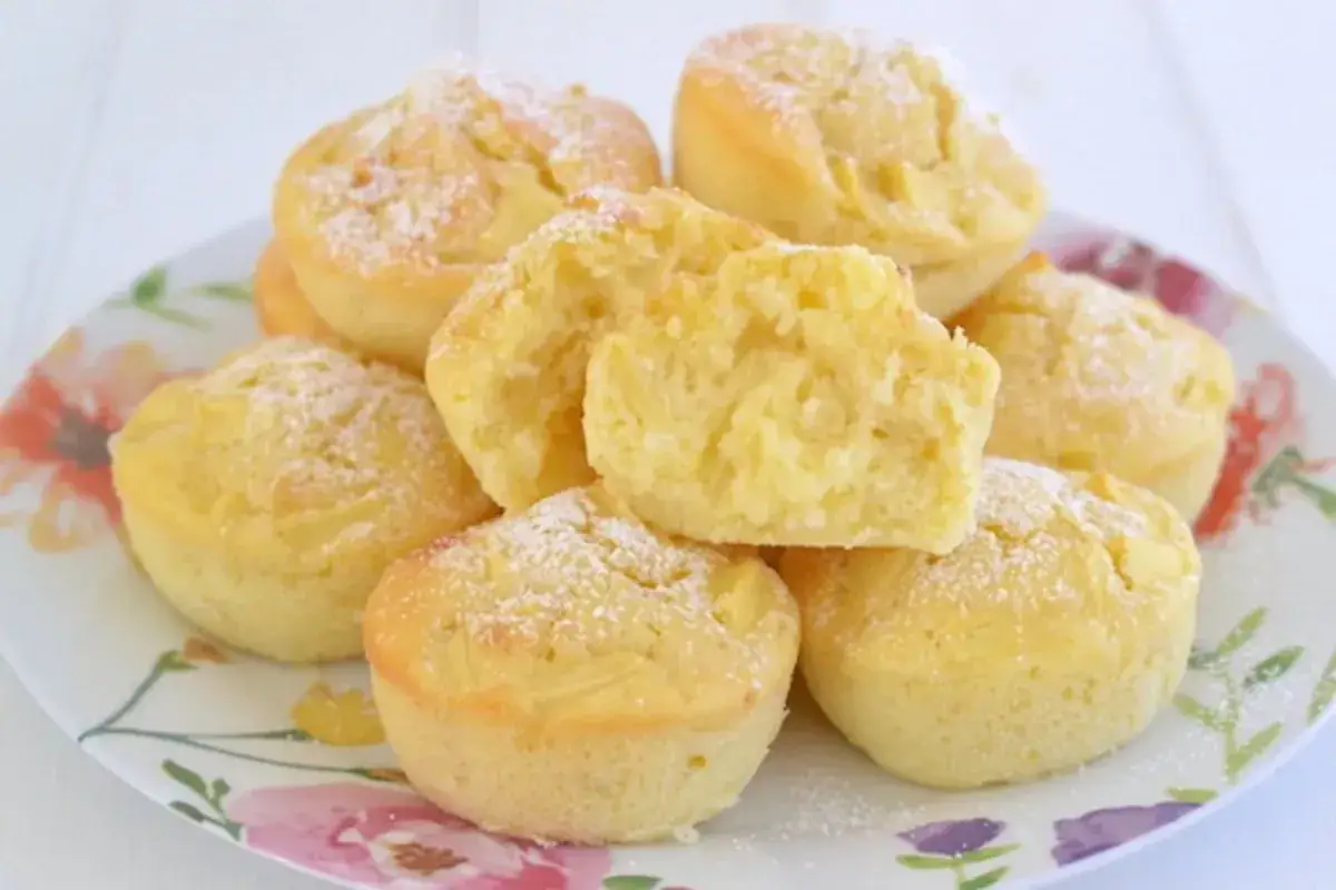 Muffin alle mele soffici e dorati, spolverati di zucchero a velo, su un piatto fiorito.