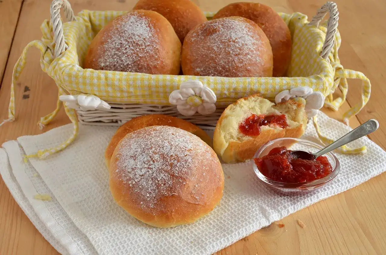 Brioches fatte in casa, soffici e spolverate di zucchero a velo, pronte per essere farcite con marmellata.