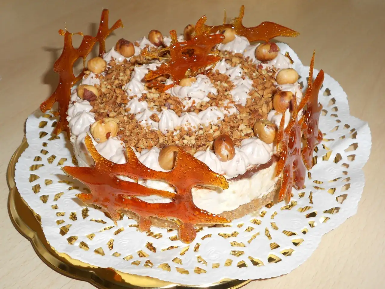 Cheesecake alla Nutella decorata con nocciole intere, granella croccante e decorazioni di caramello ambrato.