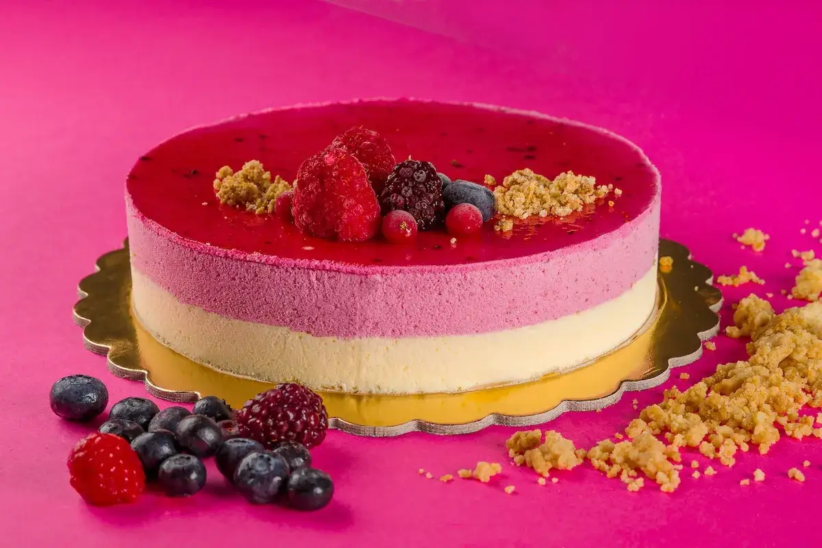 Torta gelato e semifreddo ai frutti di bosco, con strati rosa e bianchi, guarnita con lamponi, mirtilli e briciole croccanti.