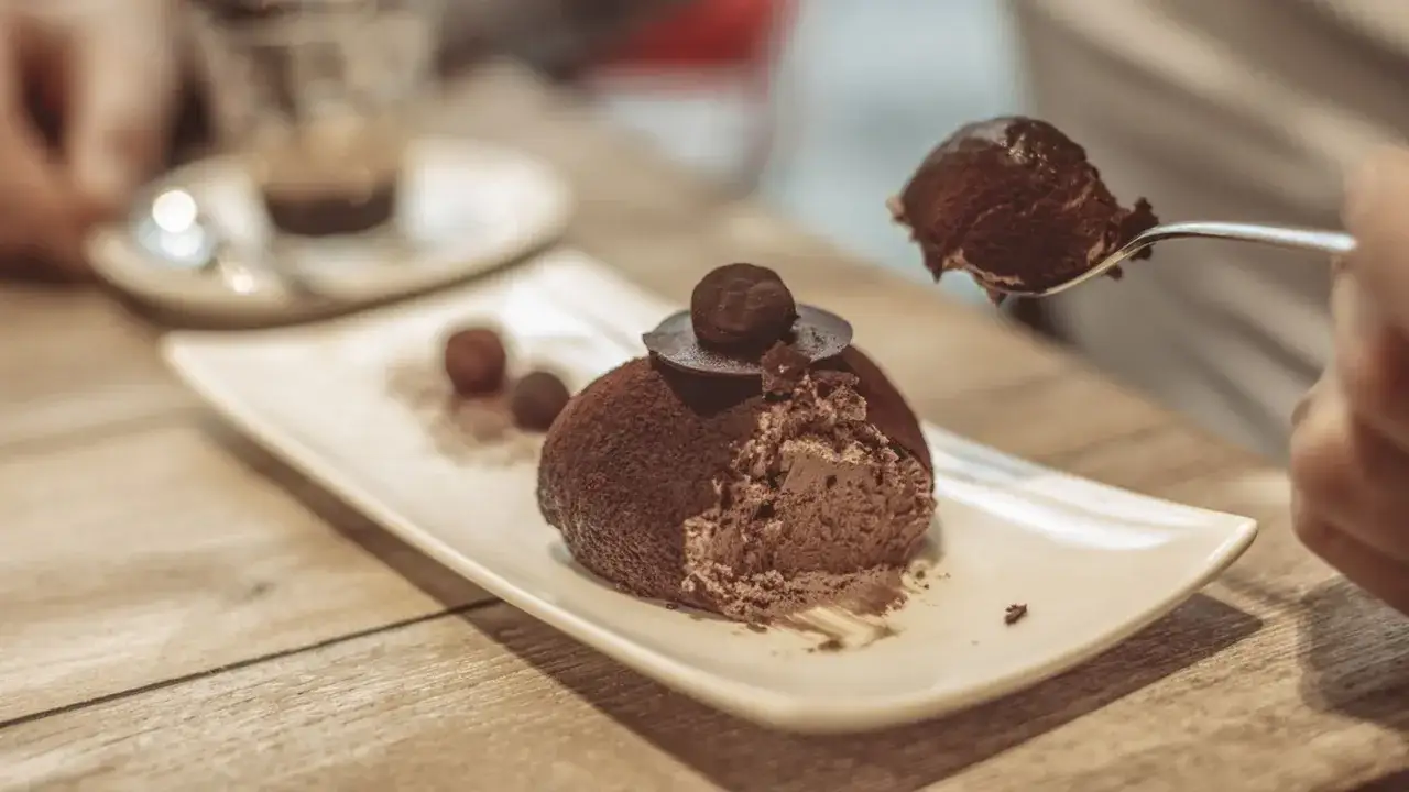 Un delizioso tartufo alla nocciola, ricoperto di cacao, viene gustato con un cucchiaino. Altri tartufi e una tazzina di caffè completano la scena.