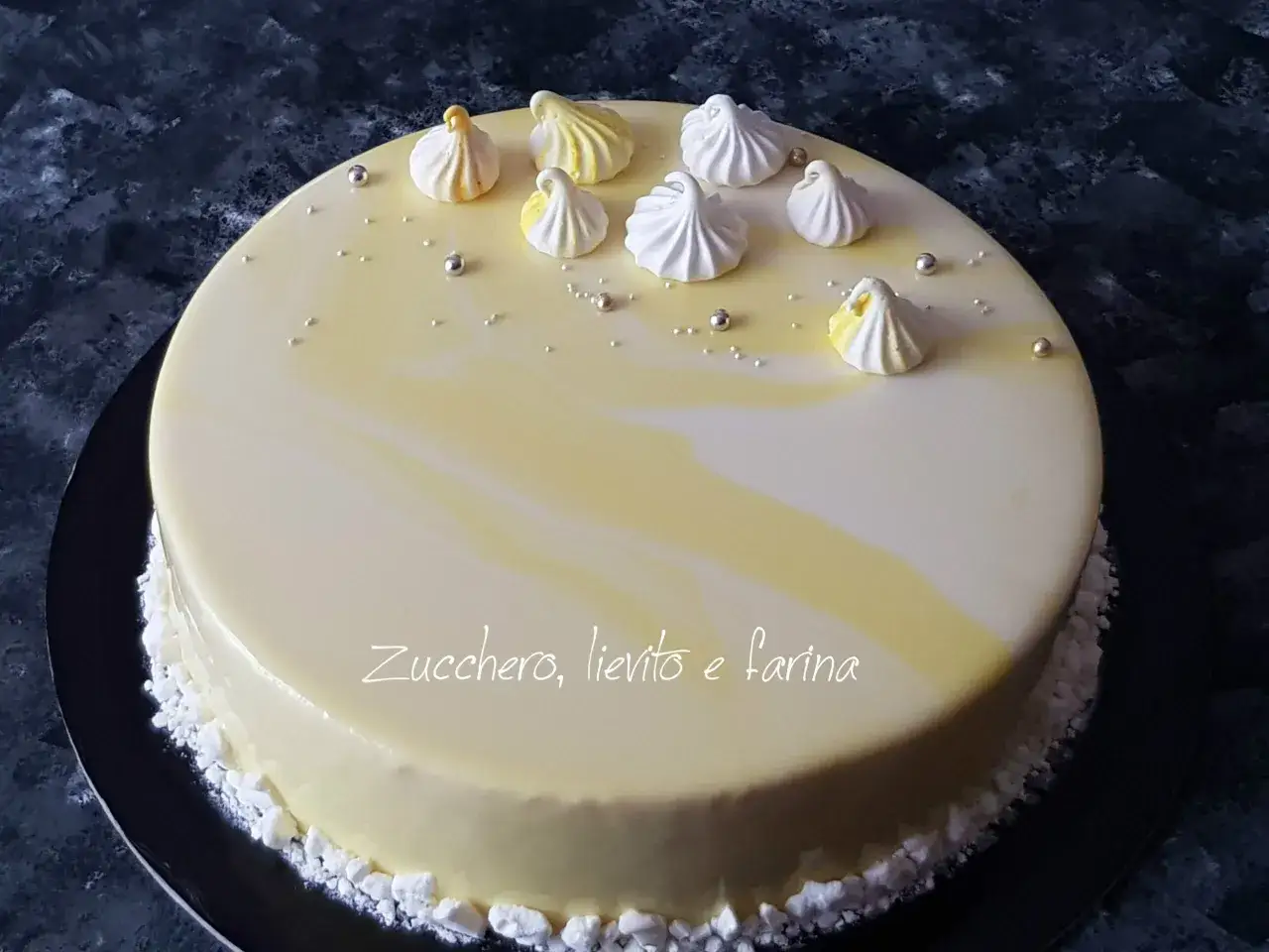 Torta con glassa a specchio gialla e bianca, decorata con meringhe e perline argentate.