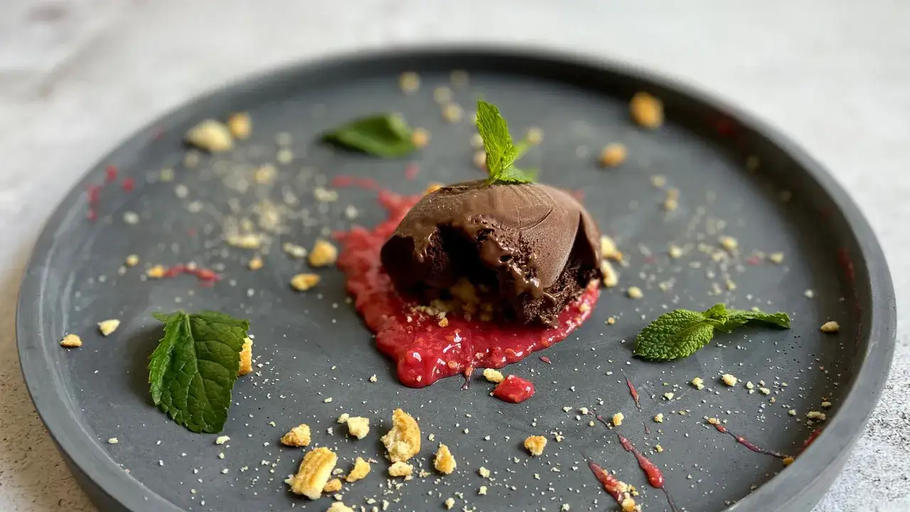 Un delizioso gelato cioccolato su un letto di salsa ai frutti rossi, guarnito con menta e briciole croccanti.