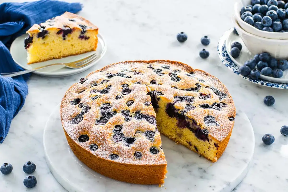 Torta yogurt vasetti con mirtilli, soffice e profumata, cosparsa di zucchero a velo. Una fetta è già servita.