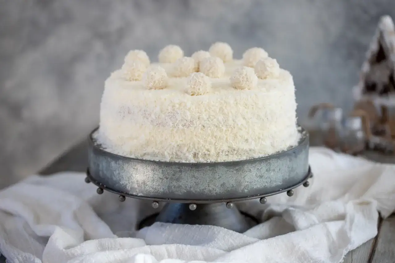 Torta Raffaello ricoperta di cocco, decorata con palline di meringa e cocco. Un dolce invitante e leggero.