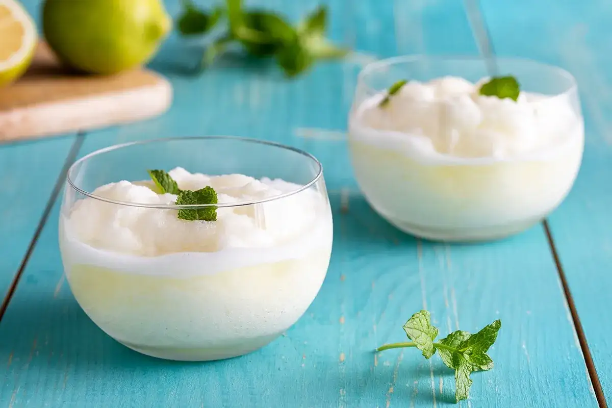 Due bicchieri di sorbetto al limone alcolico, guarniti con menta fresca, su un tavolo di legno blu.
