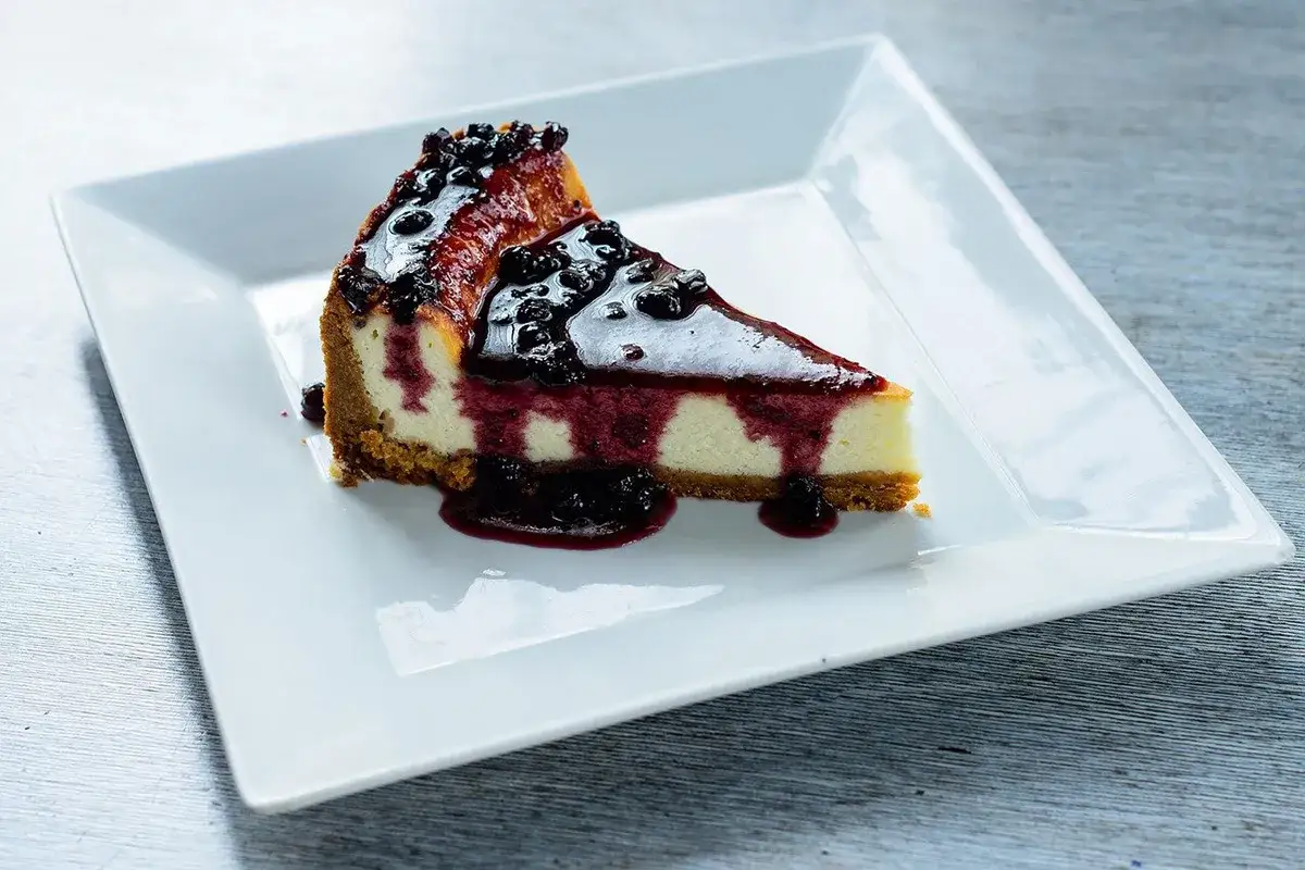 Una fetta di cheesecake con yogurt greco, ricoperta da una glassa lucida e frutti di bosco.