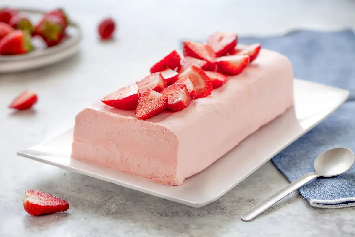 Delizioso semifreddo alle fragole, guarnito con fragole fresche, servito su un piatto bianco con un cucchiaino.