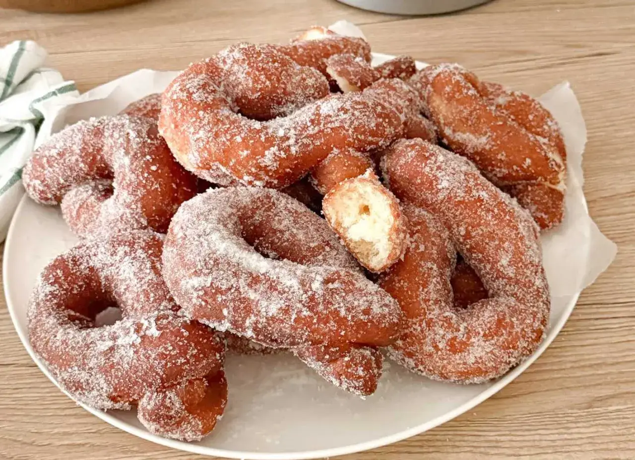 Un mucchio di ciambelle fritte, dorate e cosparse di zucchero, invitano a un morso goloso.