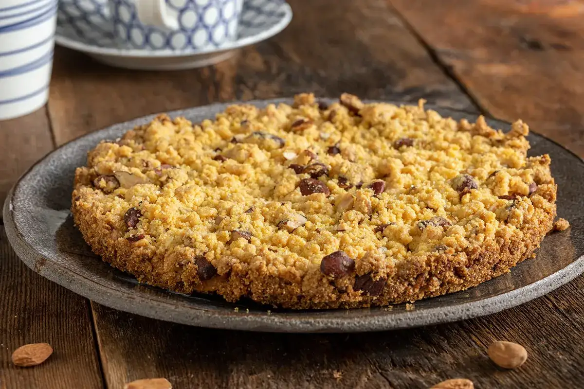 Sbrisolona ricetta: torta sbriciolata con mandorle e nocciole su piatto scuro, pronta da gustare.