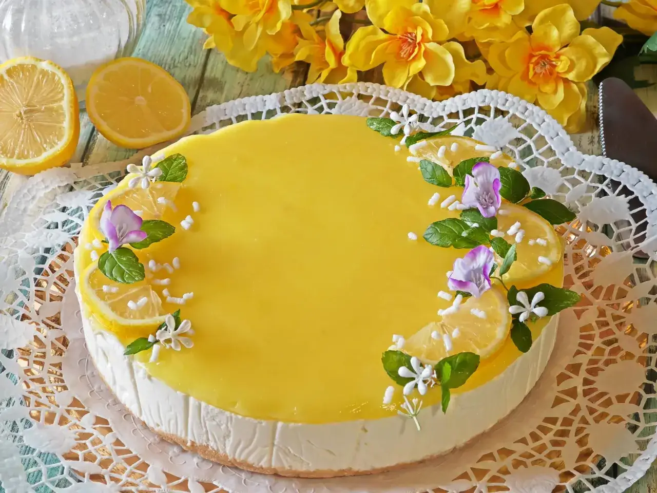 Cheesecake al lime, decorata con fette di limone, menta e fiori. Un dolce fresco e profumato.