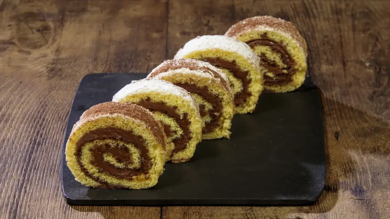 Fette di rotolo alla nutella cosparse di zucchero a velo e cacao, su una lavagna scura, pronte per essere gustate.
