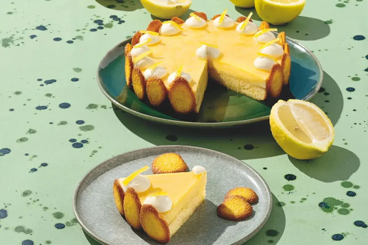 Torta con crema al limone, decorata con meringhe e scorzette, servita su un piatto con una fetta.