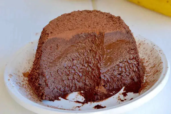Dolce banana e cioccolato: una torta soffice e cremosa, ricoperta di cacao, servita su un piatto bianco.