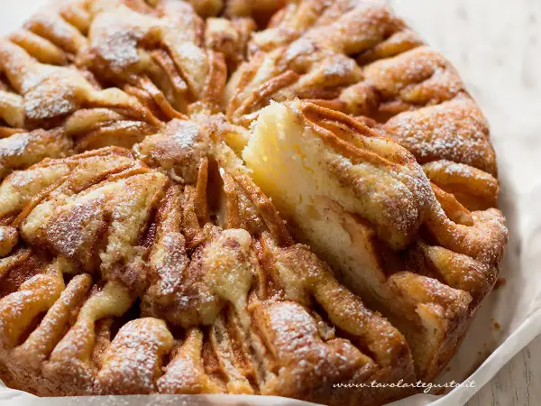 Una deliziosa torta di mele, cosparsa di zucchero a velo, con una fetta appena tolta che rivela la morbidezza dell'impasto e le mele caramellate.