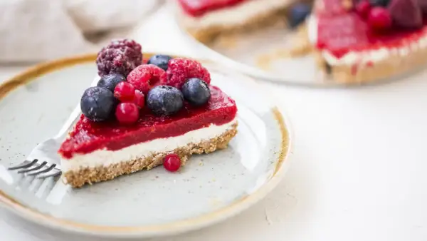Una fetta di cheesecake ai frutti di bosco, con una glassa rossa brillante e bacche fresche, su un piatto con una forchetta.