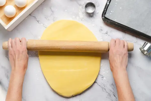 Mani stendono la pasta frolla senza burro con un mattarello. Ingredienti per dolci leggeri.
