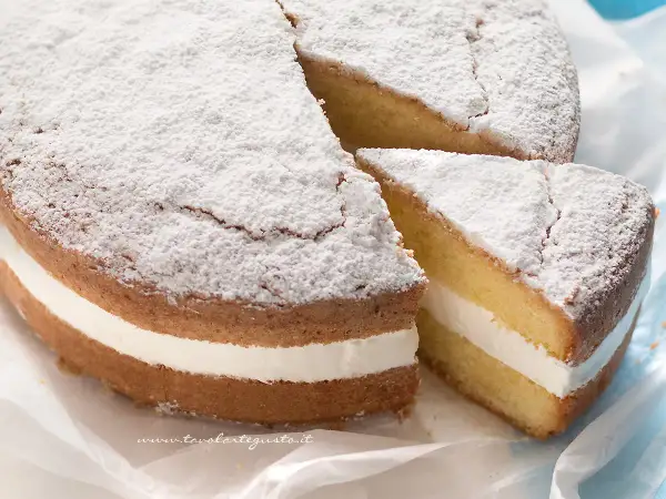 Una soffice torta kinder paradiso, spolverata di zucchero a velo, con una golosa crema bianca tra due strati di pan di Spagna.