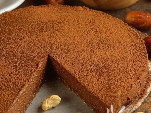 Torta al cioccolato spolverata di cacao, con una fetta mancante e anacardi a guarnire.