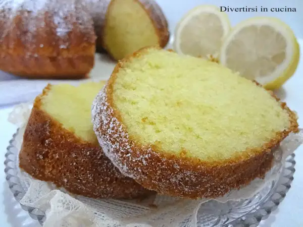 Fette di torta al limone spolverate di zucchero a velo, con fette di limone sullo sfondo.