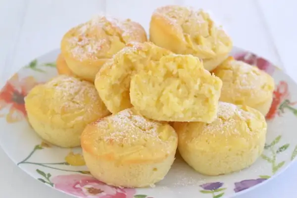 Muffin alle mele soffici e dorati, cosparsi di zucchero a velo, su un piatto fiorito. Uno è tagliato a metà, mostrando la morbida consistenza.