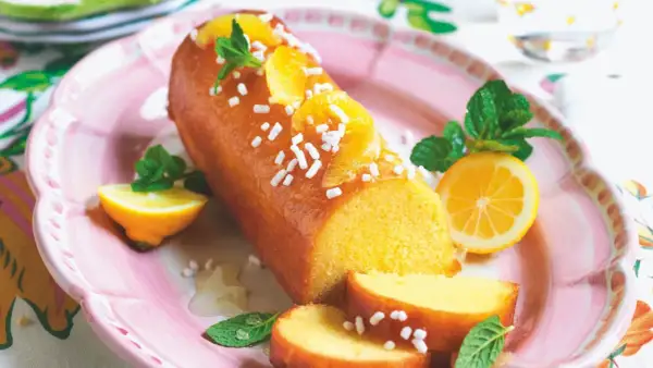 Torta facile glassata all'arancia, decorata con spicchi d'arancia, menta e zuccherini. Servita su un piatto rosa con spicchi di limone.