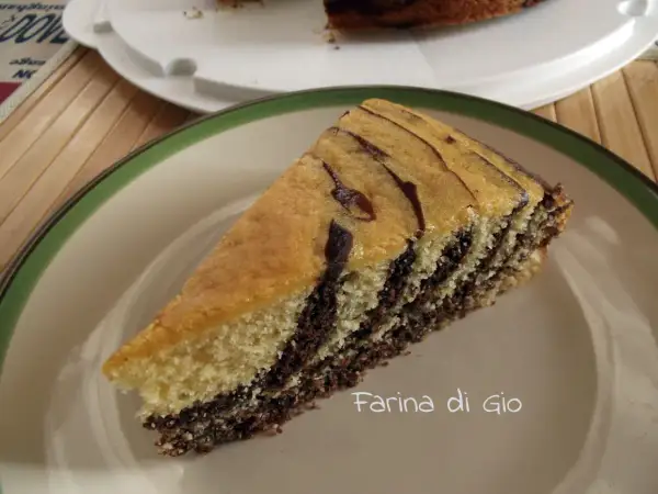 Una fetta di torta zebrata, con strati alternati di impasto chiaro e scuro, su un piatto con bordo verde.