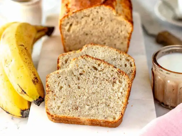 Fetta di banana bread senza uova, soffice e dorata, accanto a banane mature e un bicchiere di latte.