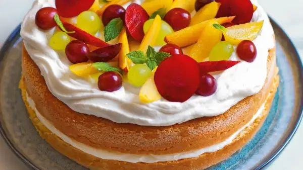 Torta con pan di spagna, panna montata e frutta fresca: uva, pesche e prugne. Un dolce estivo colorato e invitante.
