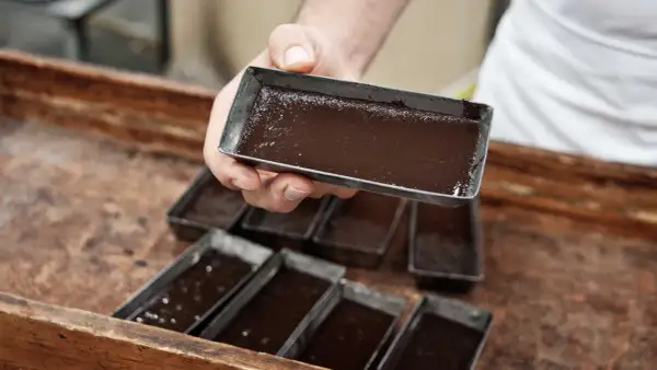Mani esperte versano cioccolato lavorato a freddo in stampini metallici, pronti per diventare delizie artigianali.