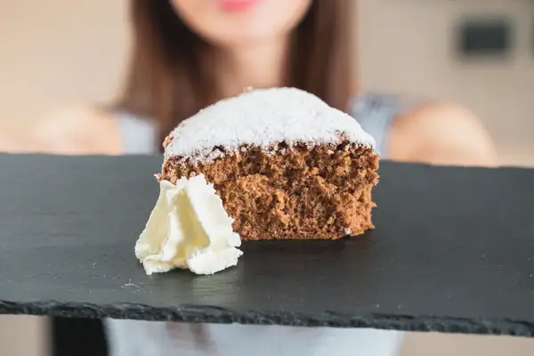 Una fetta di pan di spagna al cacao, soffice e spolverata di zucchero a velo, servita con panna montata su una lavagna scura.