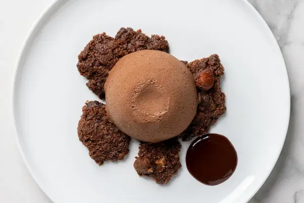Delizioso semifreddo al cioccolato su un piatto bianco, circondato da croccanti biscotti al cacao e una goccia di salsa al cioccolato.