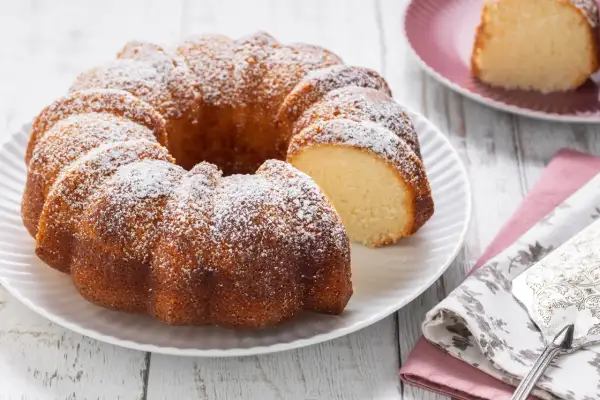 Ciambellone senza uova, soffice e dorato, spolverato di zucchero a velo. Una fetta è già stata tagliata, invitando ad assaggiarlo.