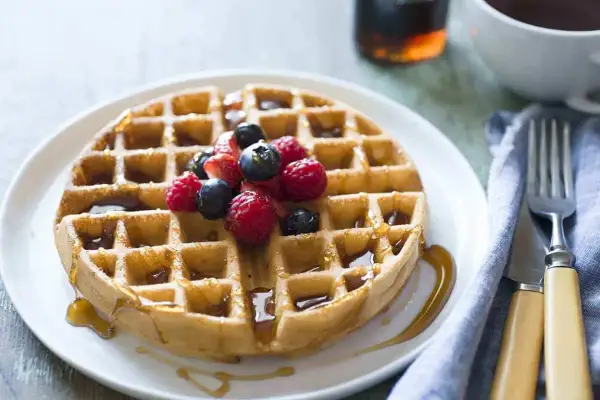 Waffle dorato con sciroppo d'acero e frutti di bosco, perfetto per una ricetta waffle golosa.