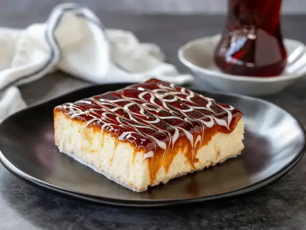Una fetta di torta trilece ricetta, bagnata da sciroppo e caramello, su piatto nero.