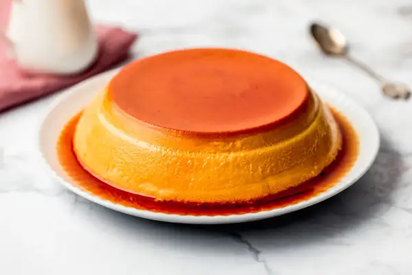 Delizioso creme caramel su un piatto bianco, con sciroppo ambrato che cola sui lati.