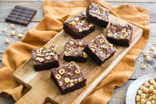Deliziosi brownies senza glutine con nocciole tostate, disposti su un tagliere di legno.