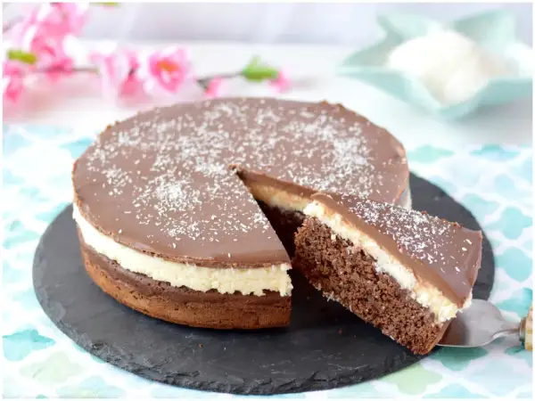 Deliziosa torta cocco e cioccolato con una fetta servita, cosparsa di cocco grattugiato.