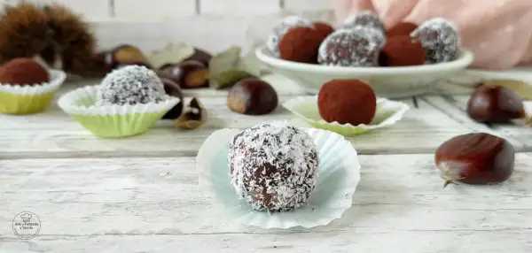 Deliziosi tartufini di castagne, alcuni ricoperti di cocco, altri di cacao, su un tavolo di legno con castagne sparse.