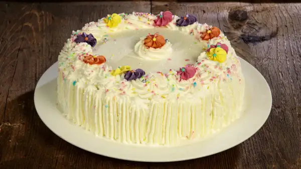 Torta compleanno uomo con panna, decorata con fiori colorati e codette, pronta per festeggiare.