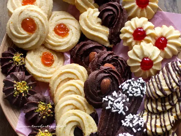 Variazioni di frolla montata: biscotti al cacao con mandorle e pistacchi, frollini con marmellata d'arancia e ciliegia, e decorati con cioccolato.
