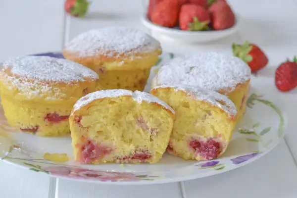 Morbidi muffin alle fragole, spolverati di zucchero a velo, invitano a un dolce assaggio. Pezzi di fragola succosa si intravedono nell'impasto soffice.