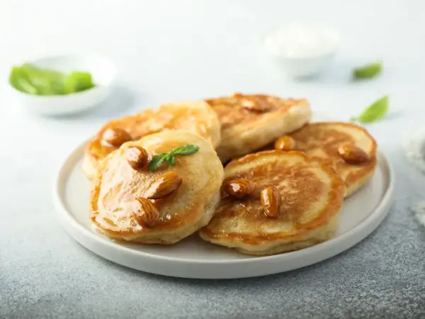 Pancakes con farina di mandorle, guarniti con mandorle intere e sciroppo dorato, su un piatto bianco.