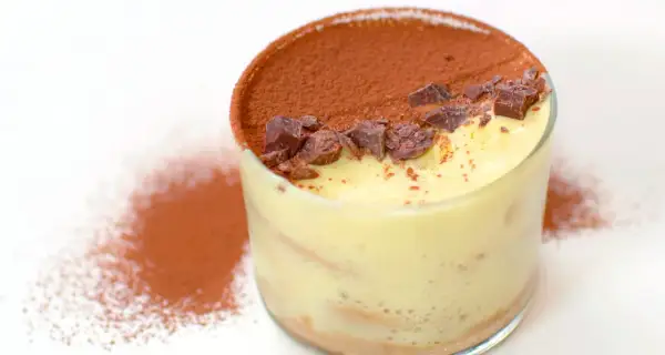 Delizioso tiramisù con crema pasticcera, cacao e scaglie di cioccolato in un bicchiere.