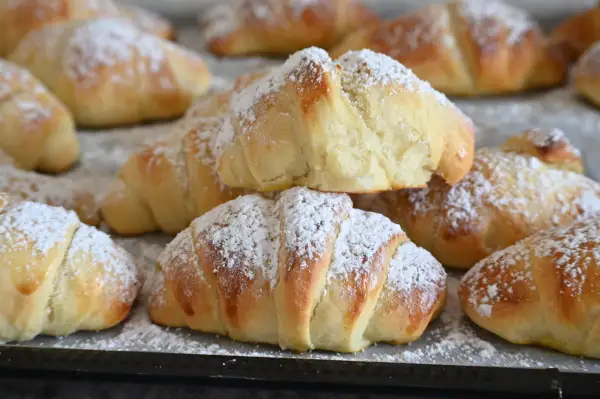 Brioches fatte in casa, dorate e soffici, cosparse di zucchero a velo. Un profumo invitante che ricorda la colazione della domenica.