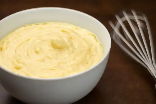 Crema pasticcera senza glutine, liscia e vellutata, pronta per farcire dolci. Vicino, una frusta in movimento.