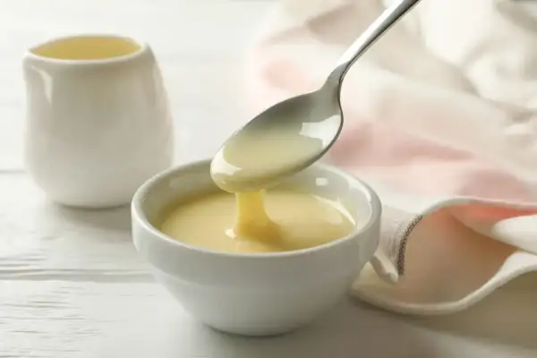 Latte condensato bimby versato da un cucchiaio in una ciotola bianca. Dolcezza cremosa pronta per dolci e caffè.