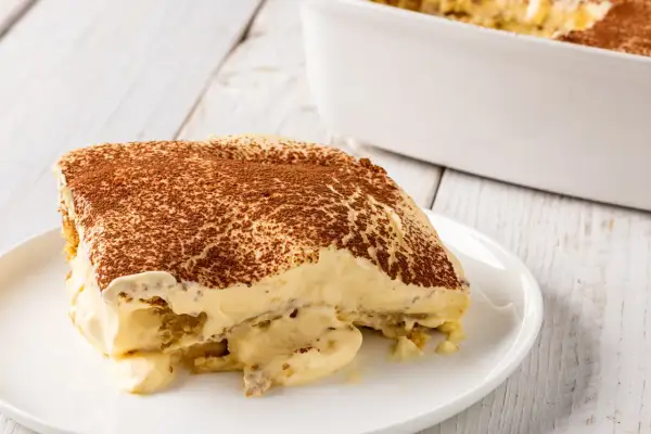 Una fetta di tiramisù, un classico dolce con mascarpone, cosparso di cacao amaro, su un piatto bianco.
